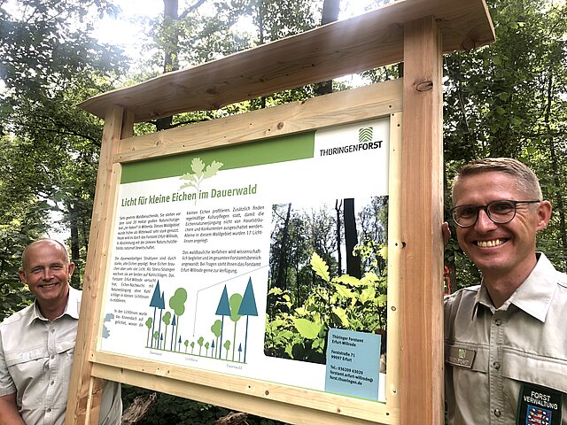 Der Forstsamtsleiter und der Revierleiter stehen vor der neuen Infointafel im Wald.