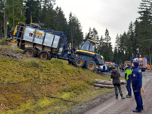 Verschiedene Einsatzkräfte stehen auf einem Waldweg und beobachten den Firefighter bei der Arbeit.